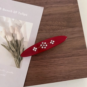 Detail view of red oval acetate hair clip with sparkling white rhinestone flower patterns