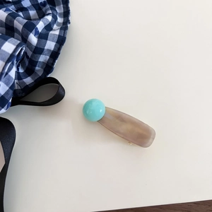 Close-up of marble pattern acetate hair clip with blue bead detail on white surface