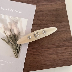 Detail of cream acetate flower hair clip with rhinestones on a wooden background