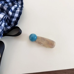 Detail of a beige marble-textured hair clip with a bright sky blue spherical accent