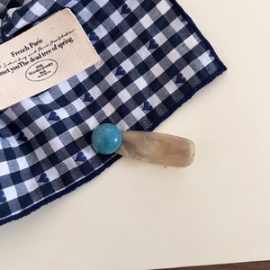 Close-up of cute ink-wash marble resin hair clip with blue bead and gold metal duckbill clamp