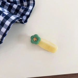Detail of yellow resin hair clip featuring a green flower with a gold sparkling rhinestone