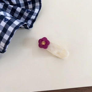 Close-up of a marble acetate hair clip with a red floral rhinestone accent on plain background