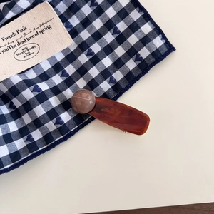 Detailed close-up of retro amber acetate hair clip with a round bead on plaid fabric