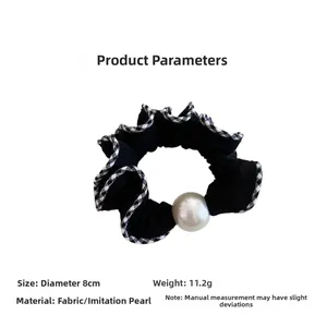 Λεπτομέρεια μαύρου scrunchie με καρό τελείωμα και μια μεγάλη λευκή στρογγυλή πέρλα