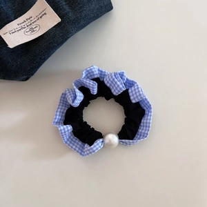 Detailed shot of blue gingham ruffled scrunchie with white pearl accent on beige surface