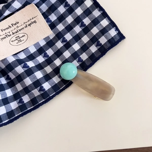 Detail of mint green bean hairpin with translucent acetate clip on a gingham fabric