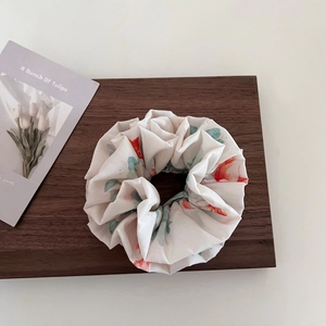 Detail view of a floral scrunchie with red and green patterns on beige fabric material