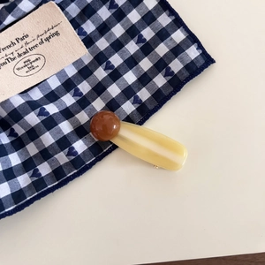 Detail view of a vintage amber resin hair clip with a brown bead on checkered fabric