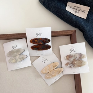 Detail of four acetate oval hair clips in tortoiseshell and marble patterns on display cards