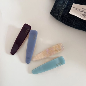 Detailed macro view of four acetate hair clips in purple, peach, and blue with gold lettering