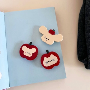 Dettaglio di tre graziose mollette per capelli a forma di mela e orsetto su un libro blu