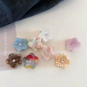 Close-up of eight acetate flower hair claws with rhinestones in various colorful patterns