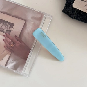 Close-up of light blue acetate hair clip with golden handmade logo on denim background