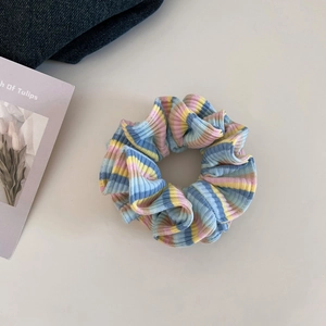 Detailaufnahme eines pastellgestreiften Haargummis auf beigem Grund mit Deko-Karte