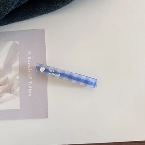 Close-up of blue checkered hair clip with Lar Mood text and silver heart detail