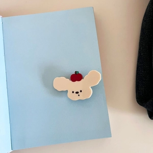 Dettaglio molletta per capelli a forma di cane crema con mela rossa su quaderno
