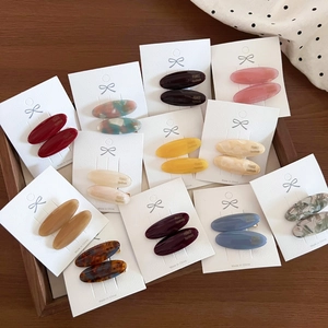 Detail view of oval acetate hair clips in assorted vintage colors on a wooden display