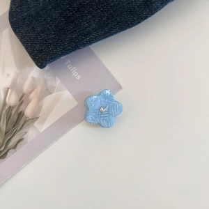 Detail of blue acetate flower hair claw with grid texture and white rhinestone center
