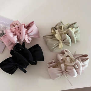 Flat lay of four satin bow hair claws in pink, black, green and beige colors on beige surface