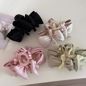 Detailed view of four satin bow hair claws in black, apricot, soft pink, and bean green colors