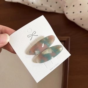 Close-up of marble acetate hair clips with handmade gold lettering on white card