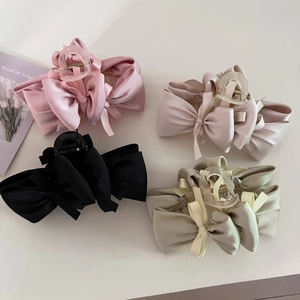 Detail view of four satin bow hair claw clips in pink, cream, black, and sage green