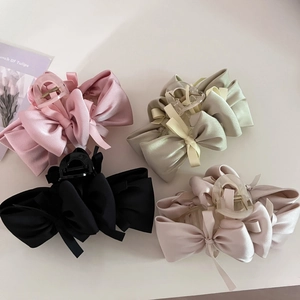 Flat lay view of four large satin bow hair claws in pink, green, black and champagne colors