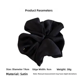 Detail view of a large black satin scrunchie with 19cm diameter and gold metal tag