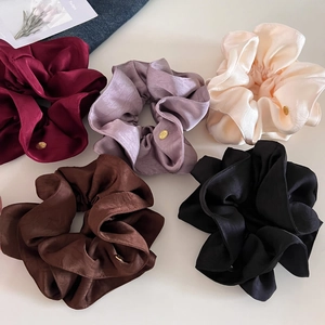 Détail de cinq chouchous en satin avec étiquettes dorées sur un fond blanc minimaliste