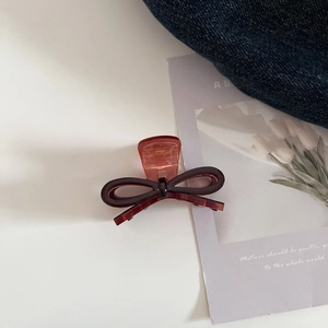 Detail of red-brown acetate bow hair claw clip placed on blue denim and art card