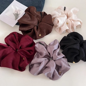 Close-up of five colorful satin scrunchies with golden labels on denim fabric