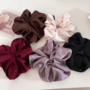 Detail of five assorted satin silk scrunchies with gold logo tags on cream surface