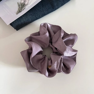Détail d'un chouchou en satin violet avec un médaillon doré sur un fond de style épuré