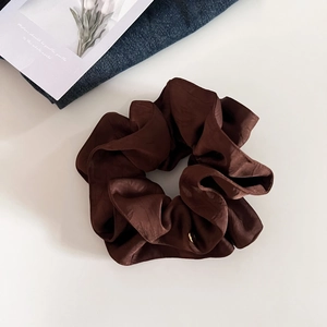 Gros plan d'un chouchou en satin marron avec des plis et un petit médaillon doré