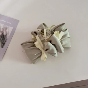 Detail of sage green satin bow hair claw clip with cream ribbon on neutral surface
