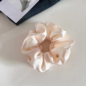 Gros plan d'un chouchou en satin crème avec des plis et un logo en métal doré