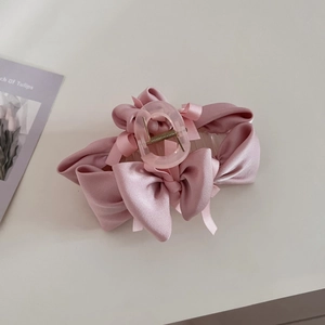 Detail view of pink satin bow hair claw clip with transparent acrylic texture and metal spring