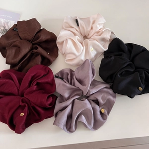 Detailed view of five satin scrunchies in various colors with golden metal charms