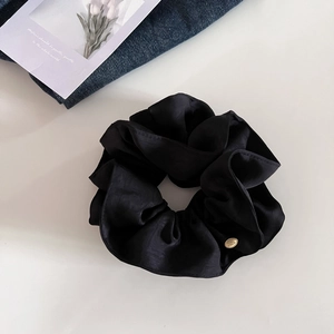 Chouchou élégant en satin noir avec breloque dorée circulaire sur fond de style de vie