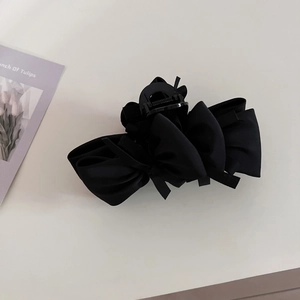 Detailed view of black satin layered bow hair claw clip on a white minimalist surface