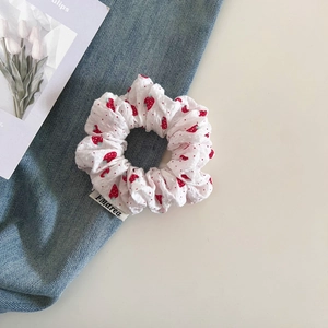 Detailed shot of white fabric scrunchie with strawberry print and brand woven label