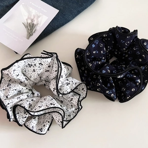 Close-up of floral ruffle scrunchies in white and blue with elegant black piped edges