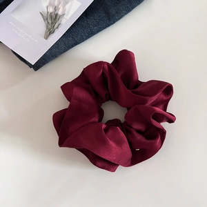 Vue détaillée du chouchou en satin rouge foncé avec des plis doux sur une surface blanche