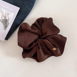 Detail of a large dark brown satin scrunchie with a gold metal logo on blue denim fabric