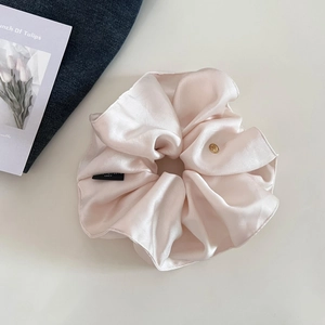 Close-up of pink satin scrunchie with a gold metal tag and elegant pleated silk texture