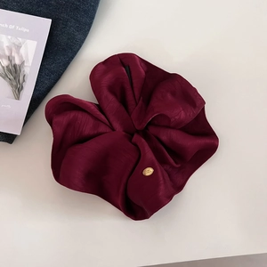 Close-up of burgundy satin scrunchie featuring a premium oval gold metal logo tag