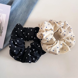 Gros plan de deux chouchous à pois en noir et beige avec un tissu en mousseline