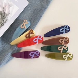 Détail de barrettes à cheveux en acétate coloré en forme de goutte avec nœud et logo doré