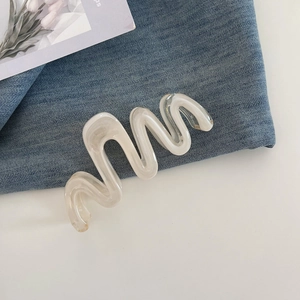 Detail showing wavy cream hair claw clip with pearlescent finish on denim texture